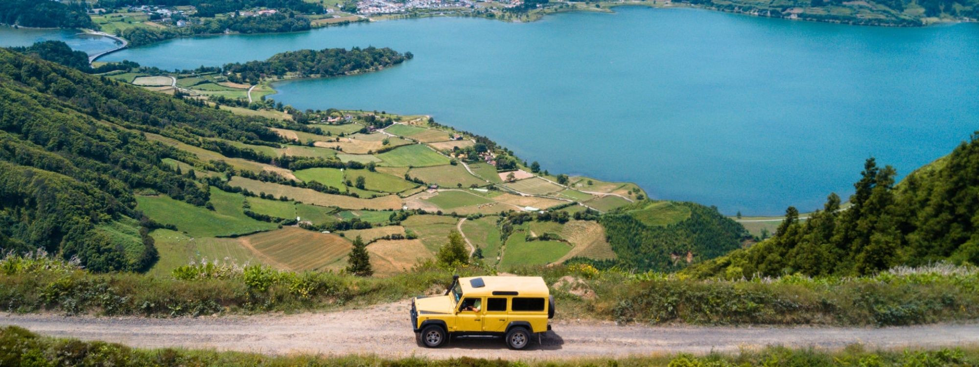 Vista panorámica de Sete Cidades en la isla de São Miguel, con las lagunas volcánicas y un coche recorriendo la carretera entre campos verdes