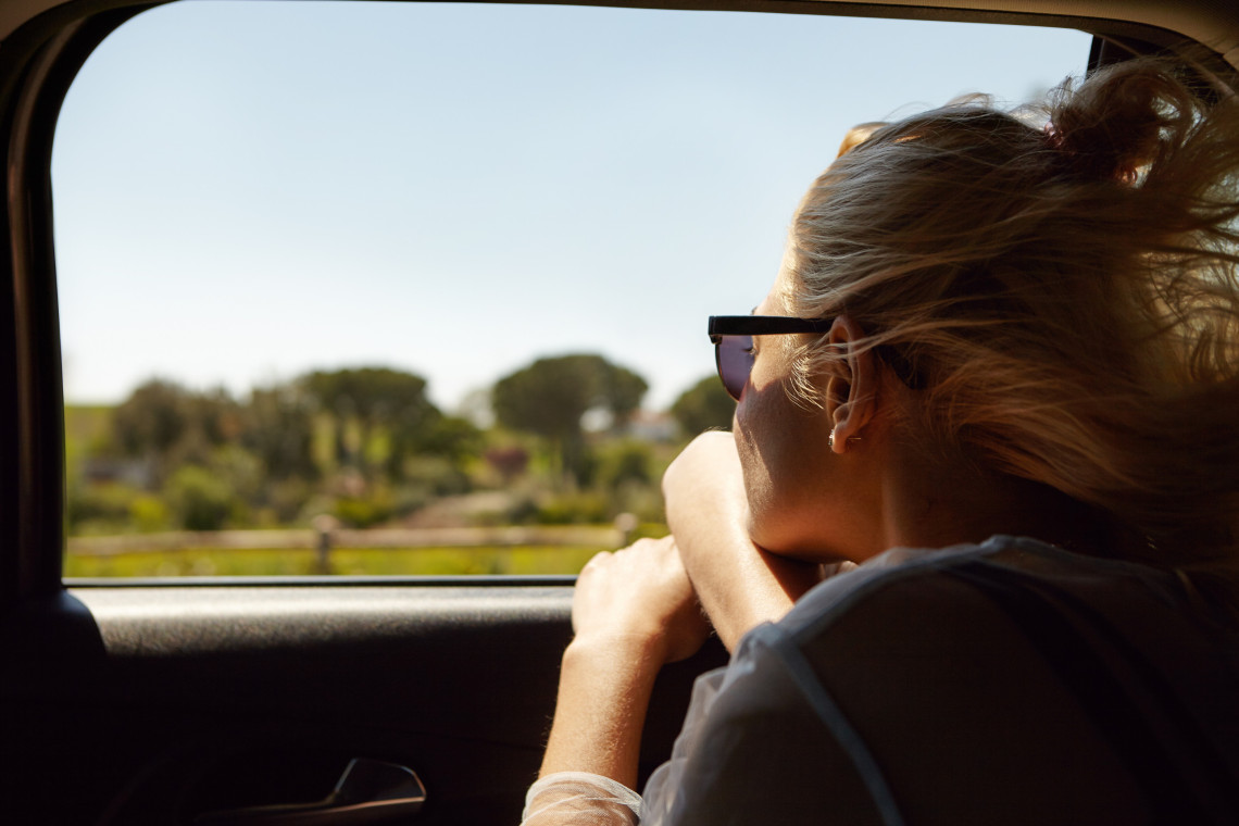Mujer viajando como pasajera en un coche por una carretera rural, disfrutando del paisaje y de la libertad de recorrer las Azores en coche