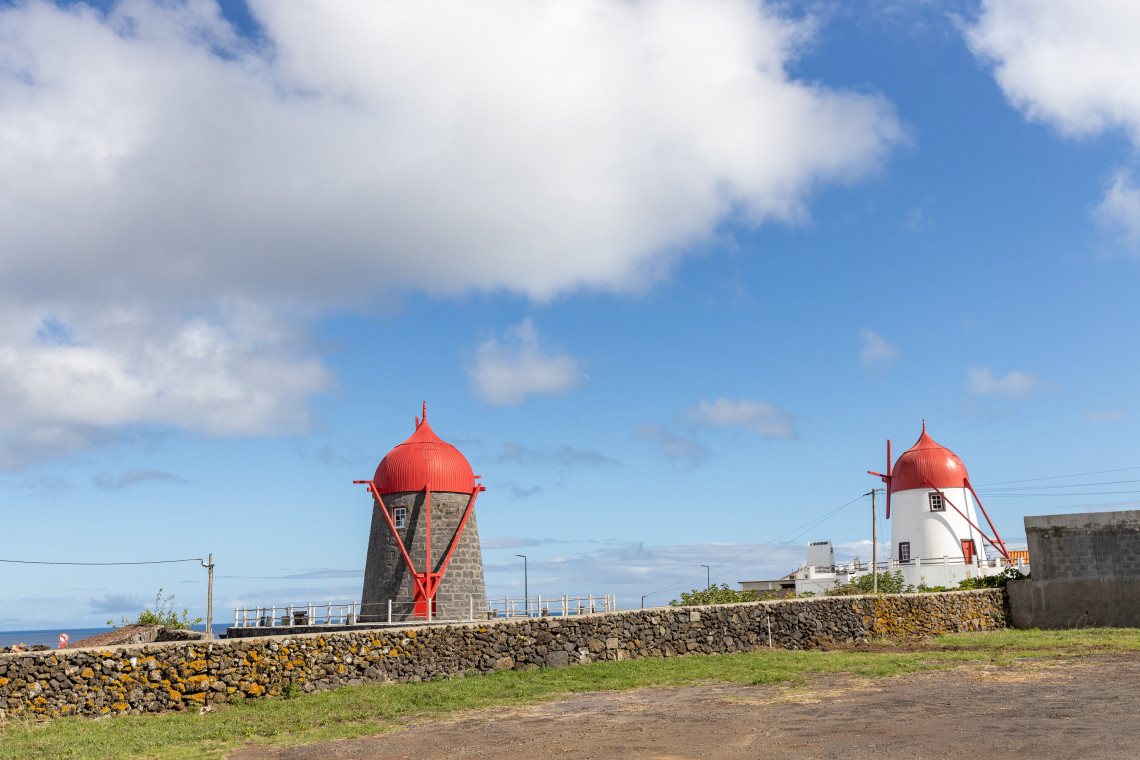 Two traditional windmills on Graciosa Island with stone and whitewashed towers topped by distinctive red wooden caps beneath a blue sky.