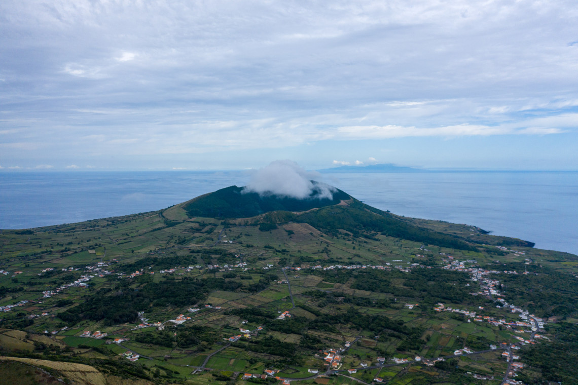 Elevated view across Graciosa Island toward the green volcanic slopes of Caldeira da Graciosa, with patchwork farmland, scattered villages and low clouds over the crater.