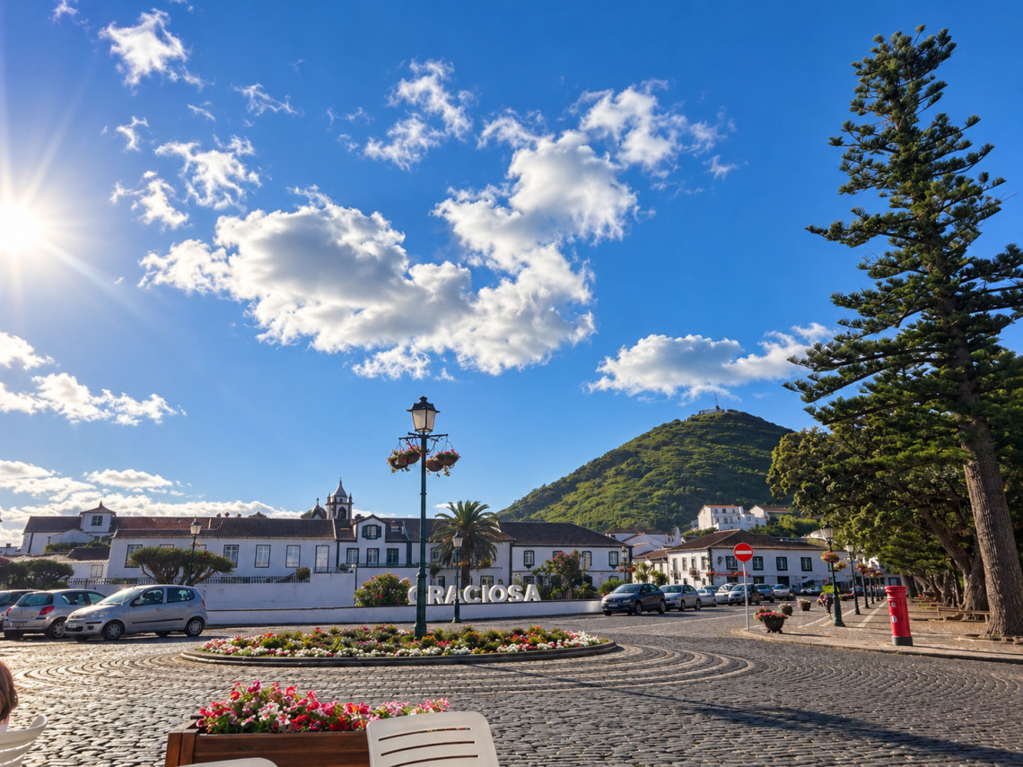 Town center of Santa Cruz da Graciosa with traditional whitewashed buildings, Portuguese cobblestone paving, landscaped flower beds and a green volcanic hill in the background.