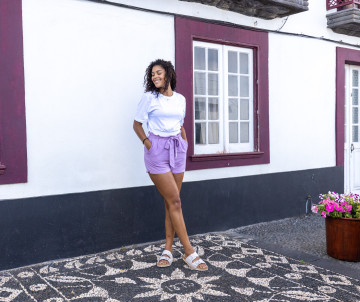 Traveler standing beside a traditional whitewashed house with dark stone trim in Santa Cruz da Graciosa, surrounded by Portuguese pavement and colorful flowers.
