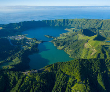 Aerial view of Sete Cidades on São Miguel Island, showing the interconnected crater lakes, village and steep green volcanic walls surrounded by the Atlantic landscape.