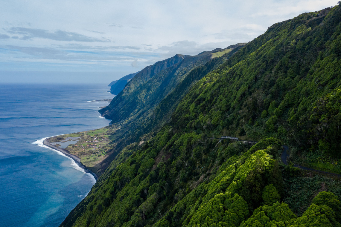 Elevated view of Faj&atilde; dos Cubres on S&atilde;o Jorge Island, showing its coastal lagoon and rural settlement beneath steep green cliffs beside the Atlantic Ocean.
