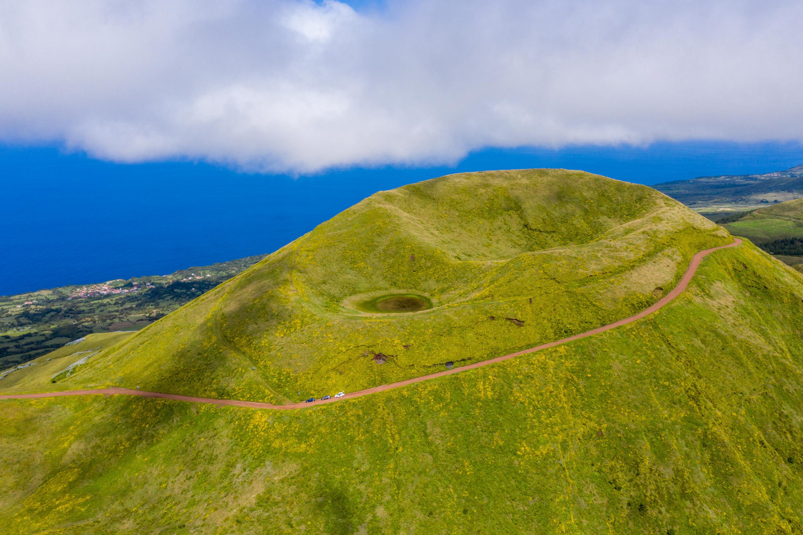 Elevated view across the green volcanic highlands of S&atilde;o Jorge Island near Pico da Esperan&ccedil;a, with a small crater and winding road above the Atlantic coast.
