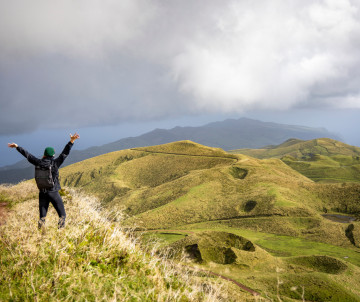 Hiker overlooking the rolling volcanic cones and grass-covered ridges around Pico da Esperança on São Jorge Island in the Azores.