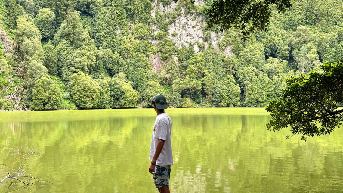 Visitor overlooking the green waters of Lagoa do Congro on S&atilde;o Miguel Island, surrounded by steep forest-covered crater walls.