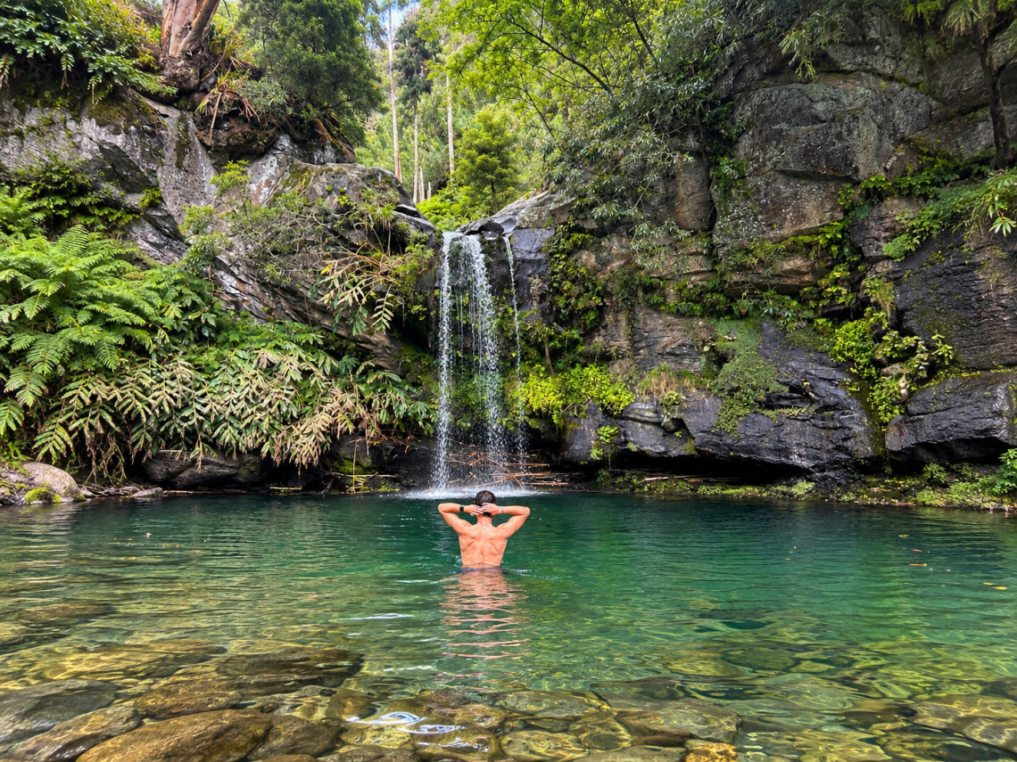 Aerial view of Cascata dos 30 Reis on S&atilde;o Miguel Island, showing twin streams of water cascading over volcanic rock into a natural pool surrounded by green vegetation.
