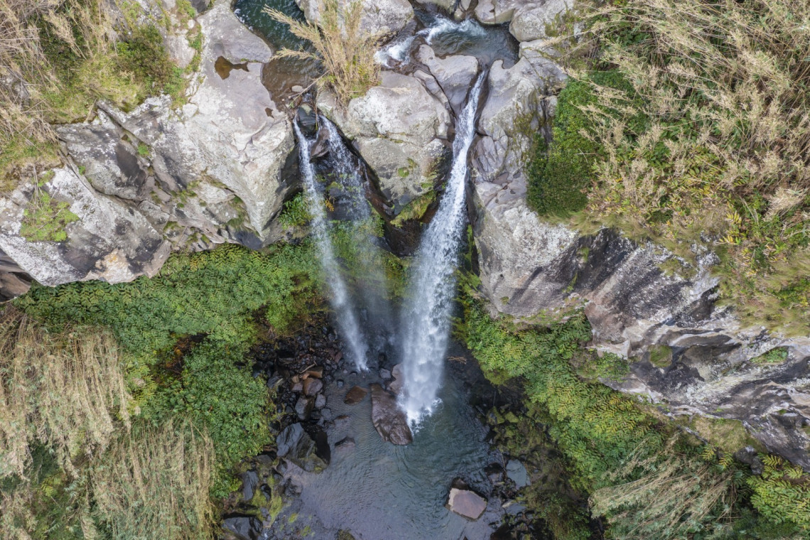 Aerial view of Salto da Farinha waterfall in Nordeste on S&atilde;o Miguel Island, with water cascading between steep volcanic rock walls into a natural pool surrounded by green vegetation.