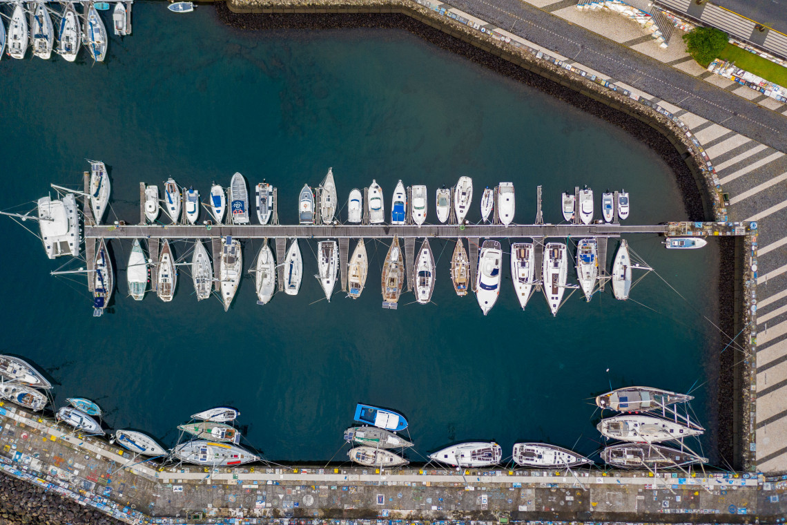 Top-down aerial view of Horta Marina on Faial Island, Azores, Portugal, showing rows of yachts moored along pontoons and the painted harbor walls.