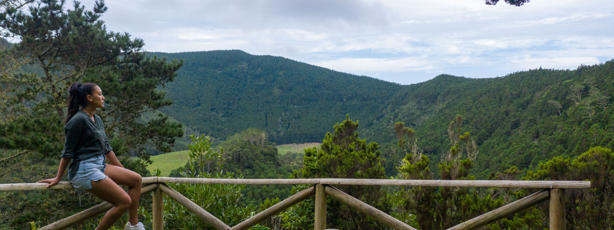 Traveler overlooking the forested interior of Caldeira da Graciosa from a wooden viewpoint on Graciosa Island, surrounded by dense green volcanic vegetation.