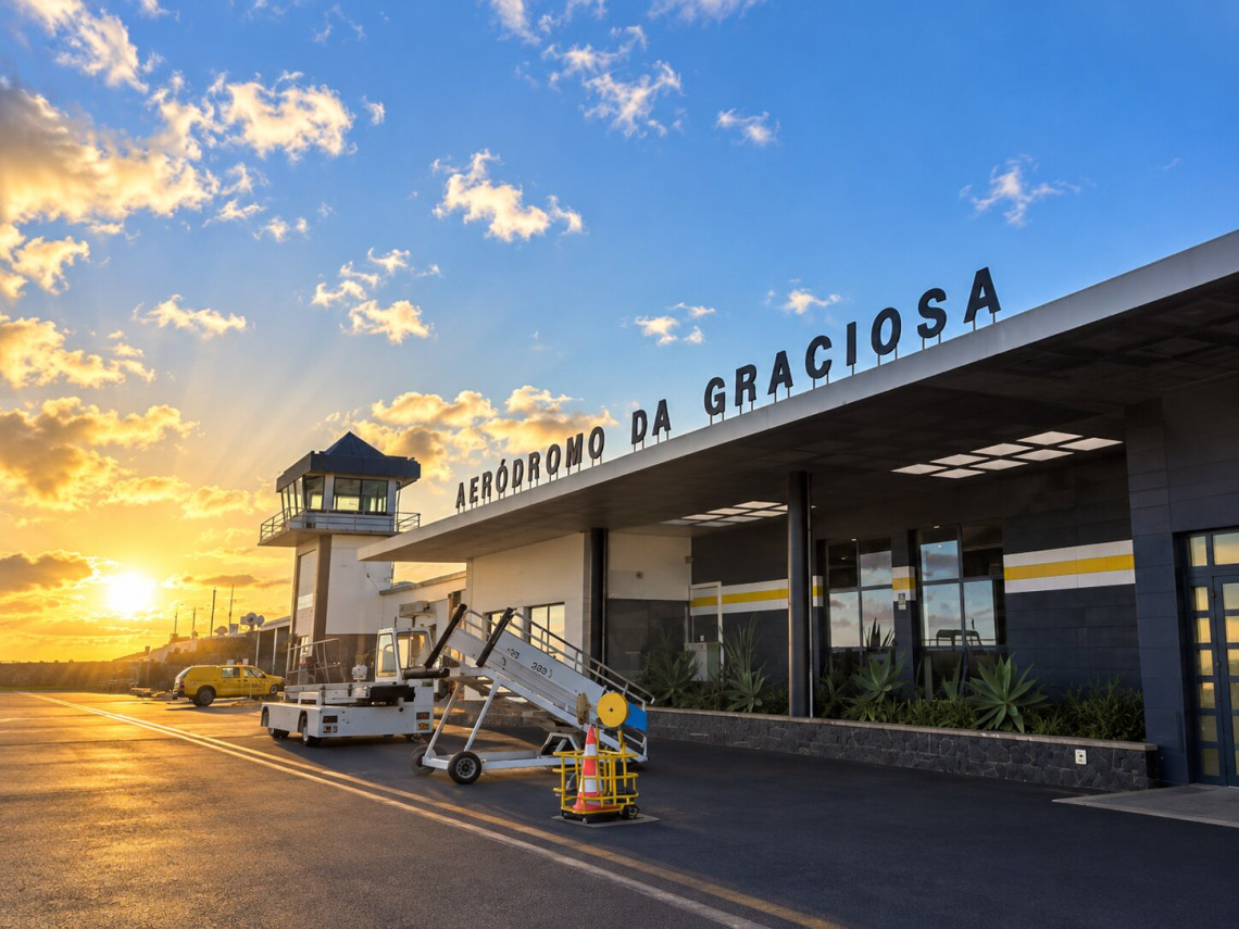 Exterior of Graciosa Airport in Santa Cruz da Graciosa during golden hour, showing the terminal, control tower and airport ground equipment beneath a blue and orange sky.