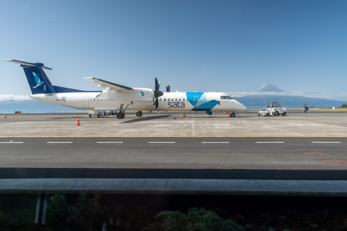 SATA Air A&ccedil;ores turboprop aircraft on the runway at S&atilde;o Jorge Airport, with the distinctive peak of Mount Pico visible across the channel.