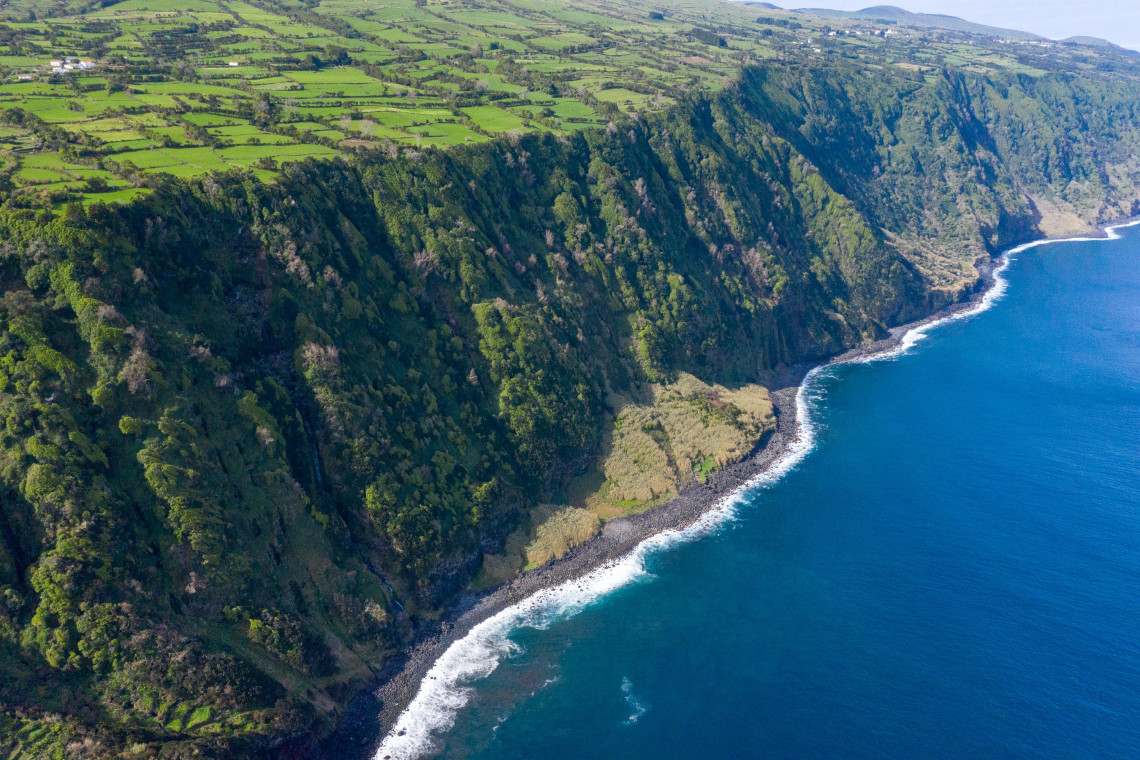 Aerial view of S&atilde;o Jorge Island&rsquo;s north coast, where green agricultural fields end at steep volcanic cliffs above the rocky Atlantic shoreline.
