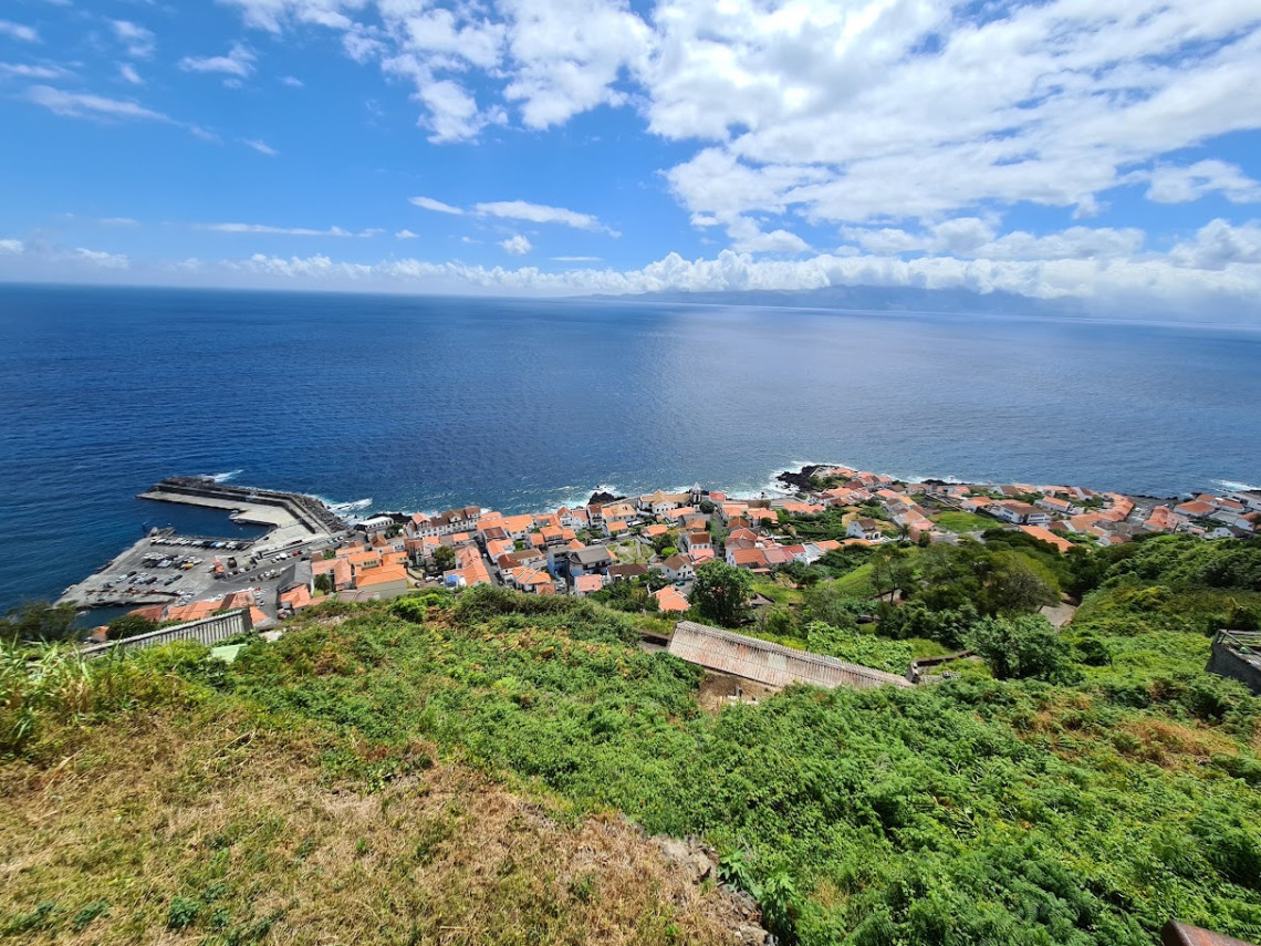 Elevated view over Velas on S&atilde;o Jorge Island, showing red-roofed houses, the coastal harbor and the Atlantic Ocean surrounded by green vegetation.