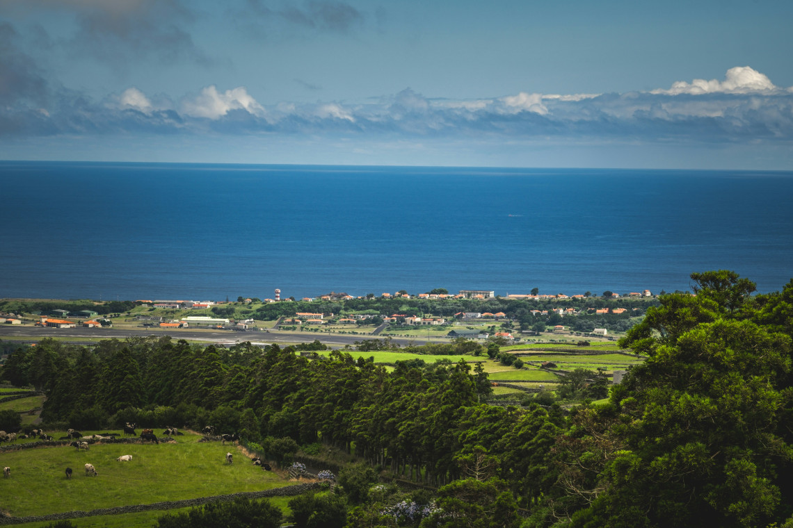 Elevated view from Serra do Cume overlooking the Lajes Plain, agricultural fields and Lajes Airport on Terceira Island. The Atlantic Ocean forms a wide blue backdrop beyond the northeastern coast.