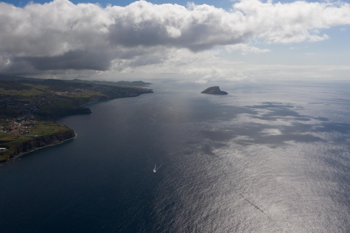 Aerial view of the southern coast of Terceira Island with the volcanic Ilh&eacute;us das Cabras rising from the Atlantic Ocean offshore. Green coastal fields and settlements follow the island&rsquo;s rugged shoreline.