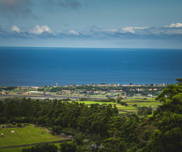 Panoramic view from Serra do Cume across the green Lajes Plain on Terceira Island, with Lajes Airport and the Atlantic Ocean visible in the distance. The viewpoint overlooks one of the broadest agricultural landscapes on the island.