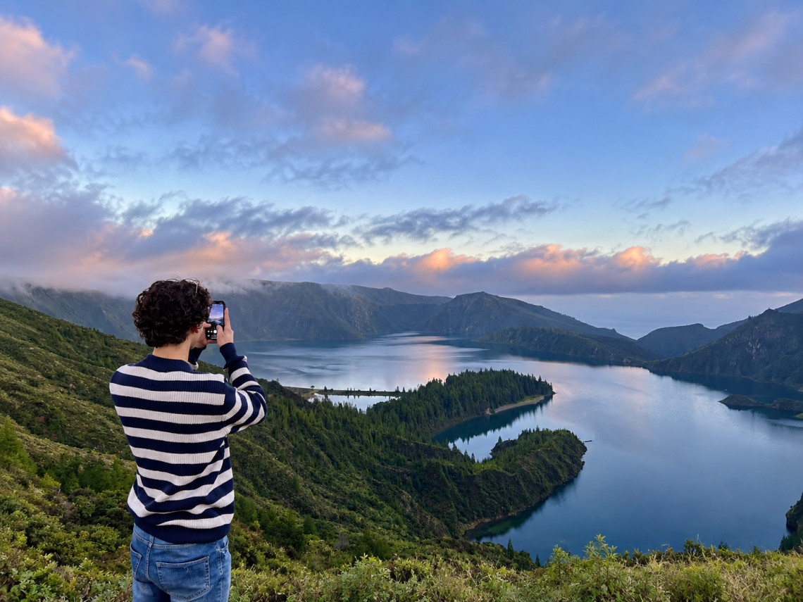 Visitor photographing Lagoa do Fogo at sunset, with the crater lake reflecting soft evening light beneath dramatic clouds and volcanic ridges.