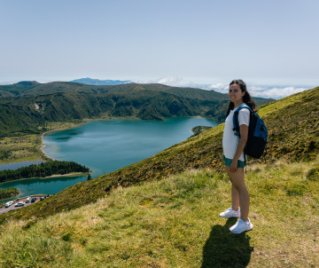 Hiker standing above Lagoa do Fogo on São Miguel Island, overlooking the blue volcanic crater lake and surrounding green mountain ridges.