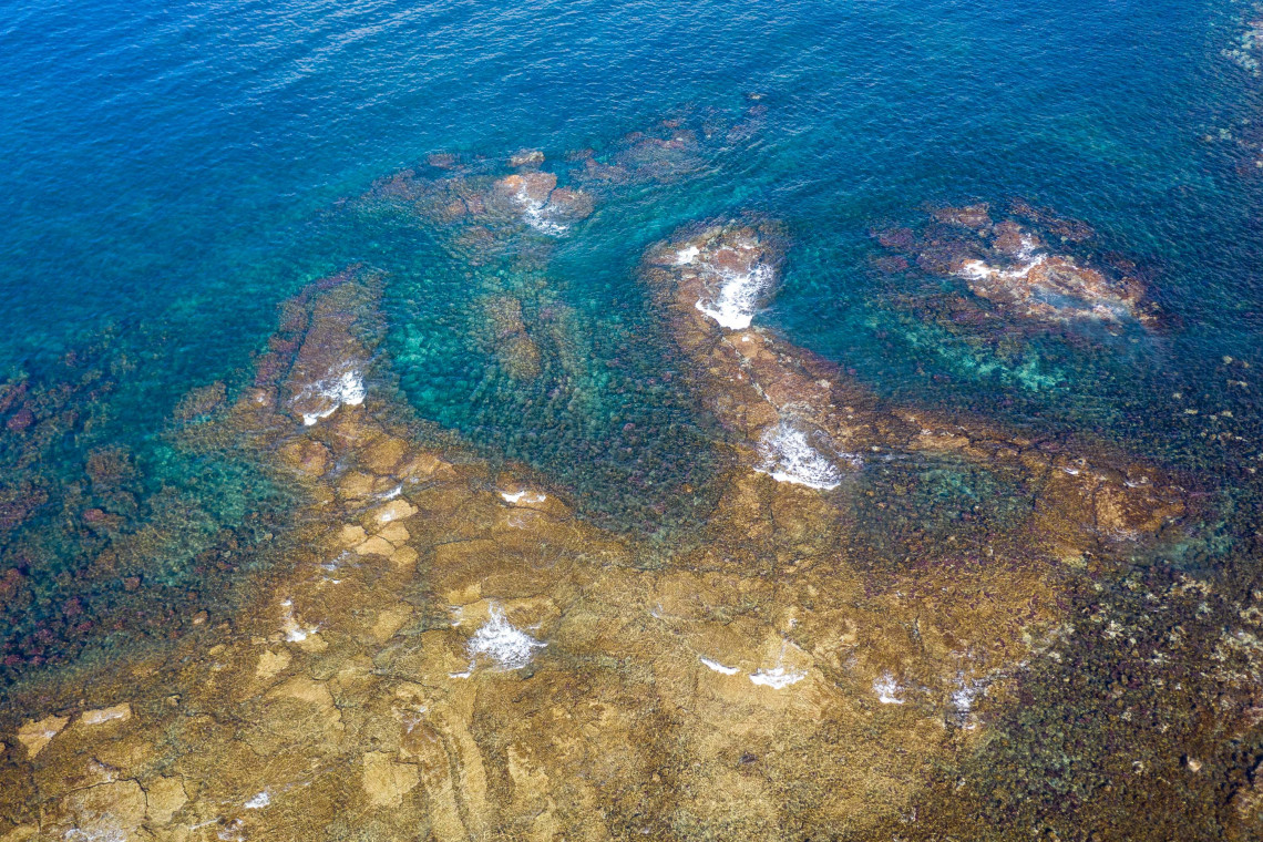 Aerial view of clear Atlantic water flowing over submerged volcanic rock formations along the coast of Pico Island.