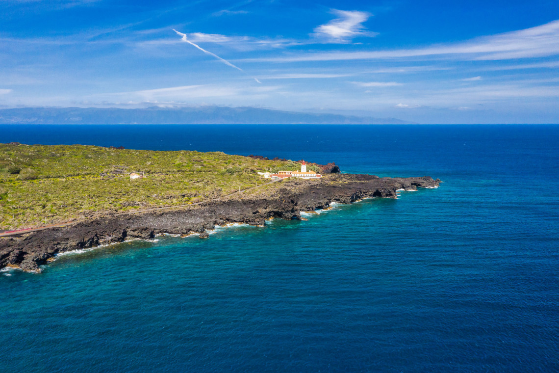 Aerial view of Ponta da Ilha Lighthouse on the eastern tip of Pico Island, surrounded by black volcanic coastline and deep blue Atlantic water.