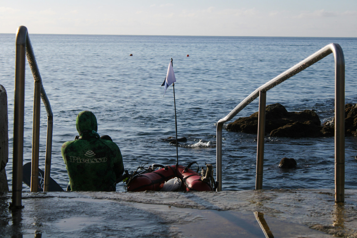 Diver preparing to enter the Atlantic Ocean from a volcanic shoreline on Pico Island, with diving equipment positioned beside the water.