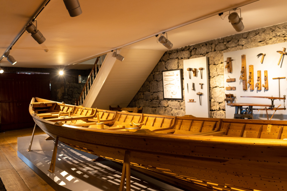 Traditional wooden whaling boat displayed inside the Museu dos Baleeiros in Lajes do Pico, with historic boat-building tools mounted on the volcanic stone walls.