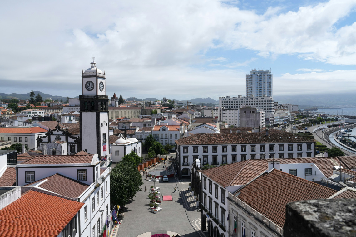 Panoramic view over central Ponta Delgada, showing traditional white buildings, red-tiled roofs, a historic clock tower and the waterfront beyond.