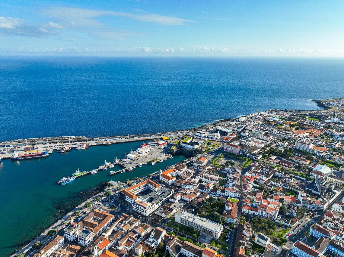 Aerial view of Ponta Delgada harbor and city center, with docks, boats, red-roofed buildings and the Atlantic Ocean surrounding S&atilde;o Miguel Island.