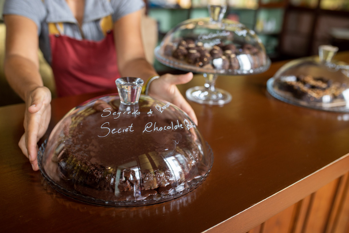 Chocolate pastry displayed beneath a glass dome at Louvre Michaelense in Ponta Delgada, with other homemade sweets arranged across the caf&eacute; counter.