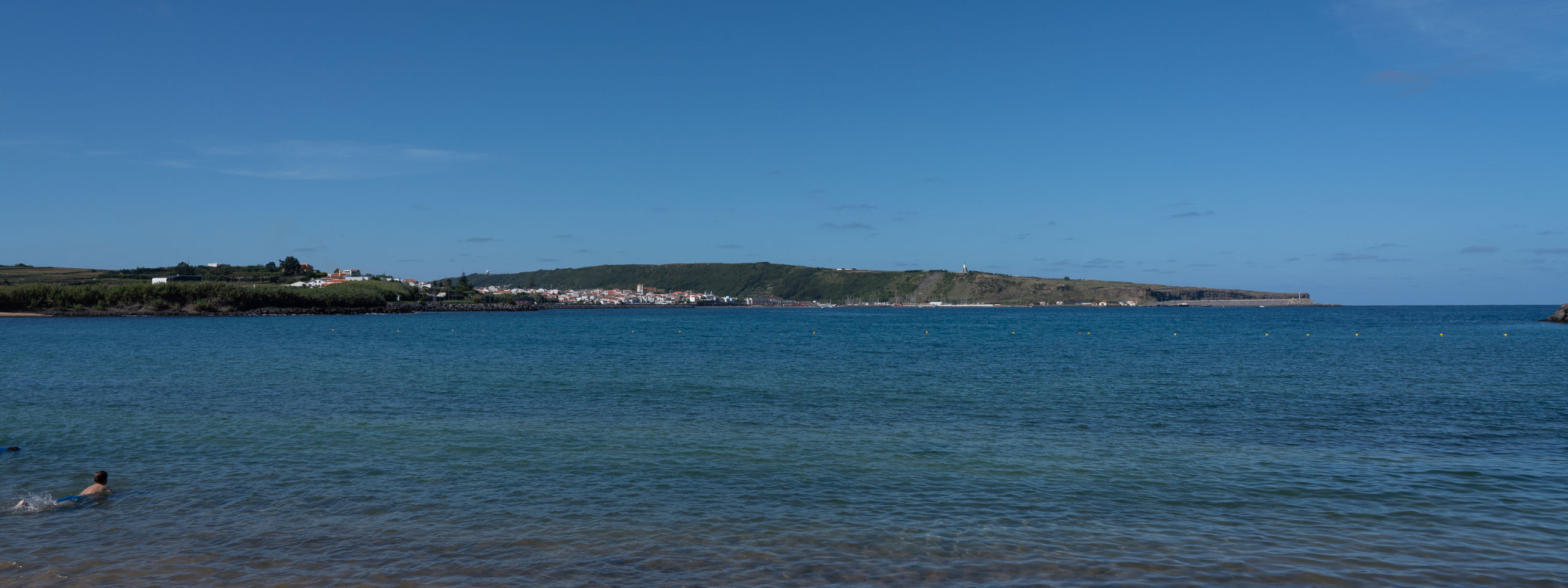 View across the calm waters of Praia da Vitória Bay on Terceira Island, with the coastline and green headland stretching across the horizon.