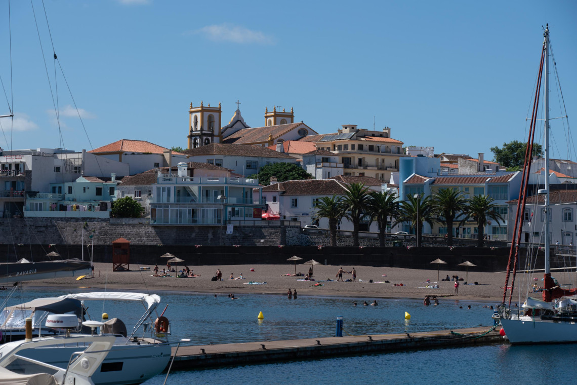 View of Praia da Vit&oacute;ria on Terceira Island, with boats in the marina, people enjoying the beach and the town&rsquo;s historic buildings and church towers rising behind the waterfront.