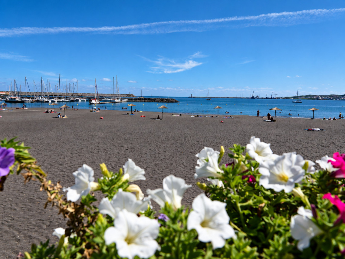 Praia Grande in Praia da Vit&oacute;ria on Terceira Island, with its broad sandy beach, calm Atlantic waters and marina framed by colorful flowers in the foreground.