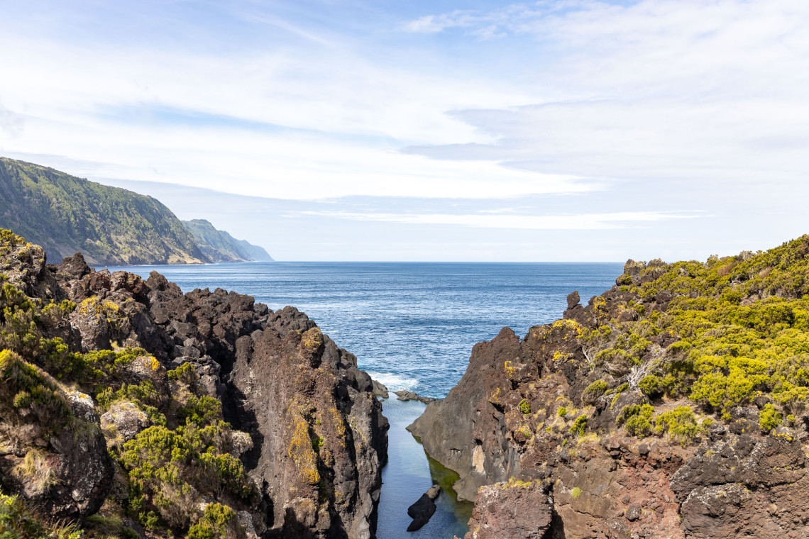 Jagged volcanic rock formations at Faj&atilde; do Ouvidor on S&atilde;o Jorge Island form a narrow natural inlet opening toward the Atlantic Ocean.