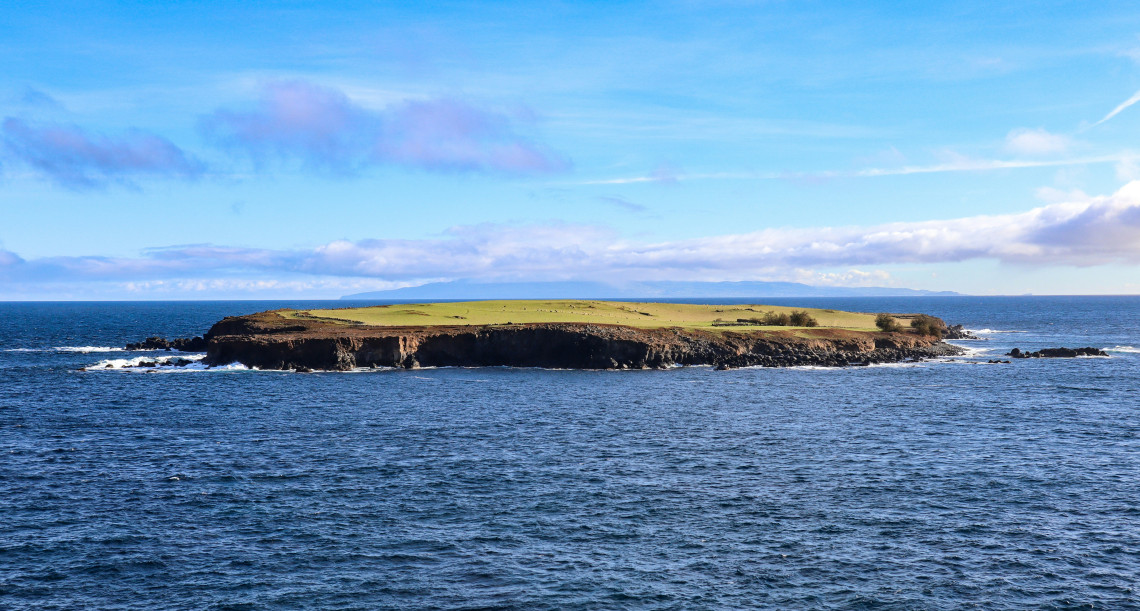 Ilh&eacute;u do Topo off the eastern end of S&atilde;o Jorge Island, a low green volcanic islet surrounded by the blue waters of the Atlantic Ocean.