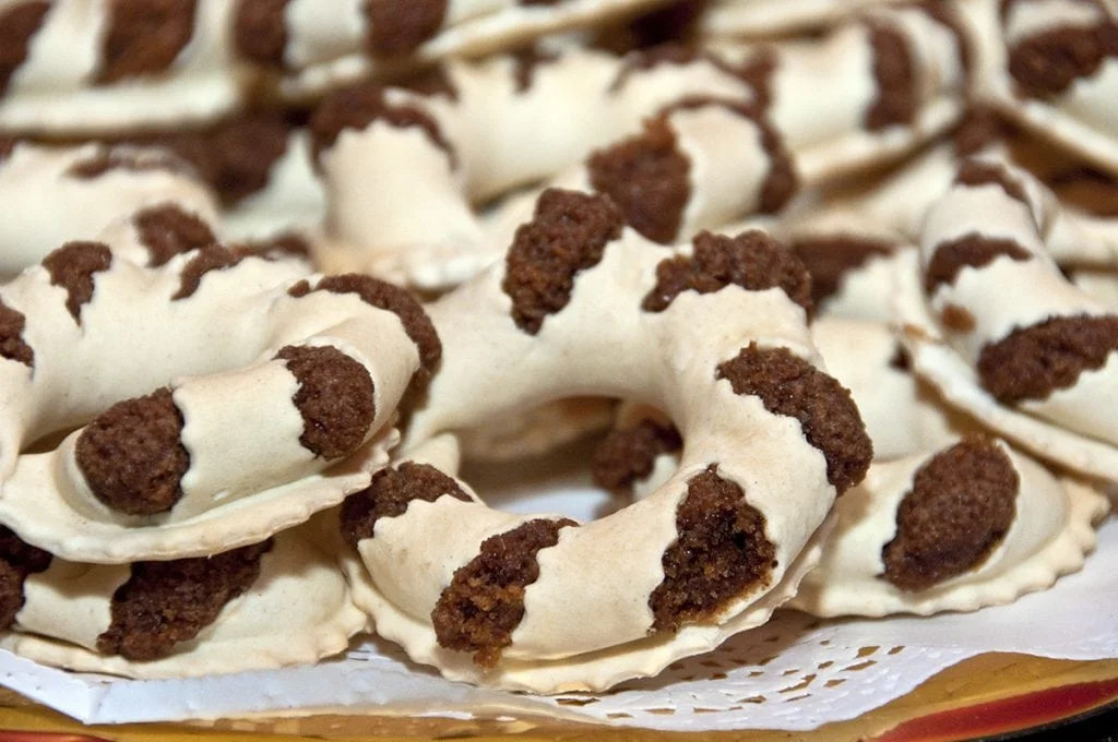 Close-up of Esp&eacute;cies de S&atilde;o Jorge, traditional ring-shaped pastries with pale dough cut to reveal their dark spiced filling.