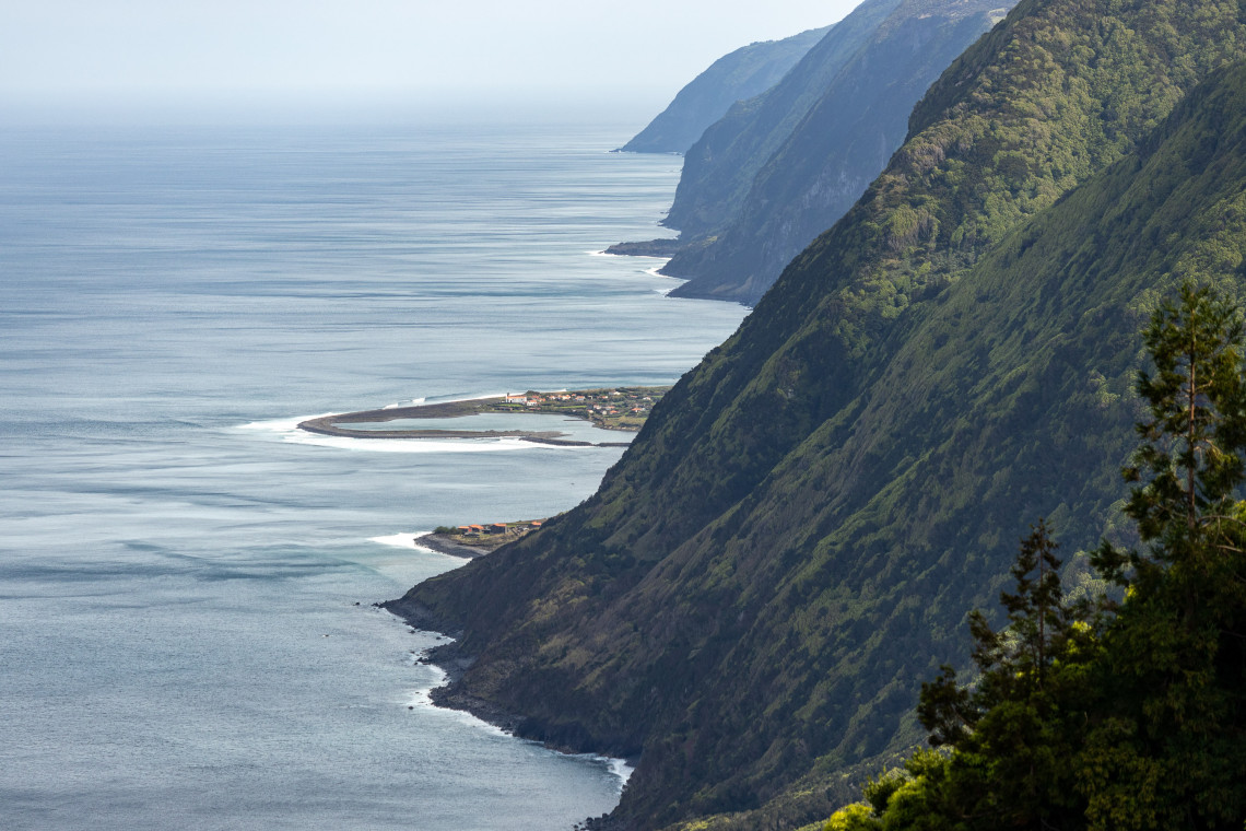 Elevated view along the north coast of S&atilde;o Jorge Island, where steep green volcanic cliffs descend toward small coastal faj&atilde;s and the Atlantic Ocean.