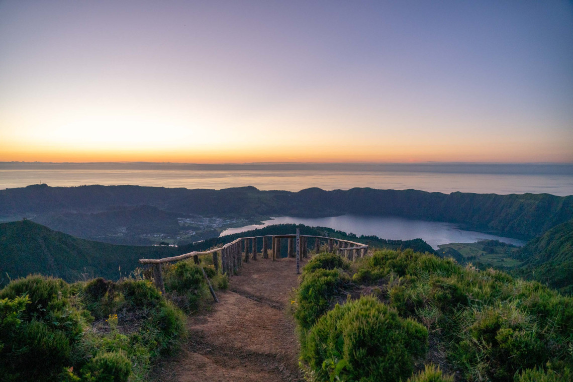 Sunset view from Miradouro da Boca do Inferno over the Sete Cidades caldera, with volcanic lakes, green ridges and the Atlantic Ocean beyond.