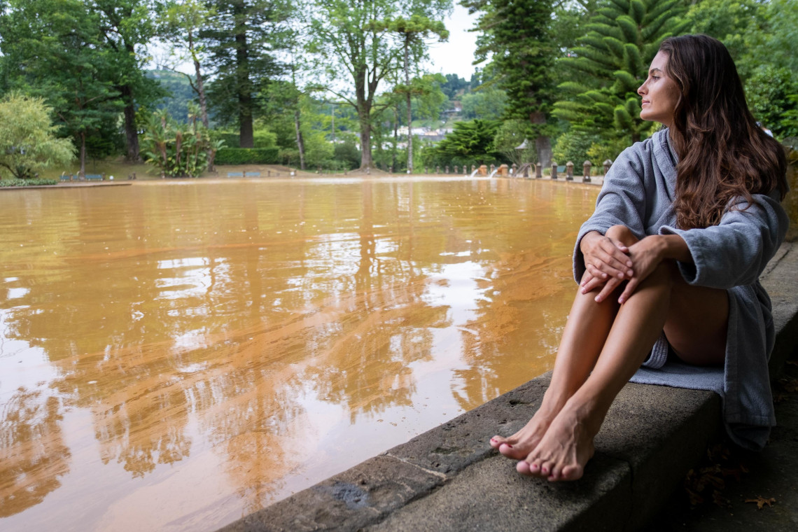 Visitor relaxing beside the large iron-rich thermal pool at Parque Terra Nostra, surrounded by mature botanical gardens in Furnas.