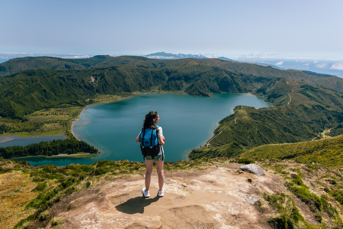 Hiker overlooking Lagoa do Fogo on S&atilde;o Miguel Island, with the blue crater lake, smaller lagoons and rugged volcanic ridges below.