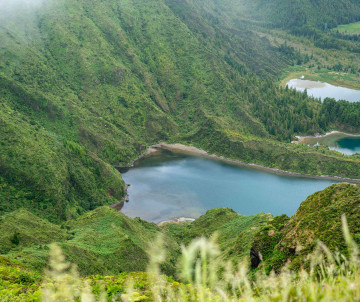 Elevated view of Lagoa do Fogo on São Miguel Island, showing the blue-green crater lake surrounded by steep volcanic slopes and lush vegetation.