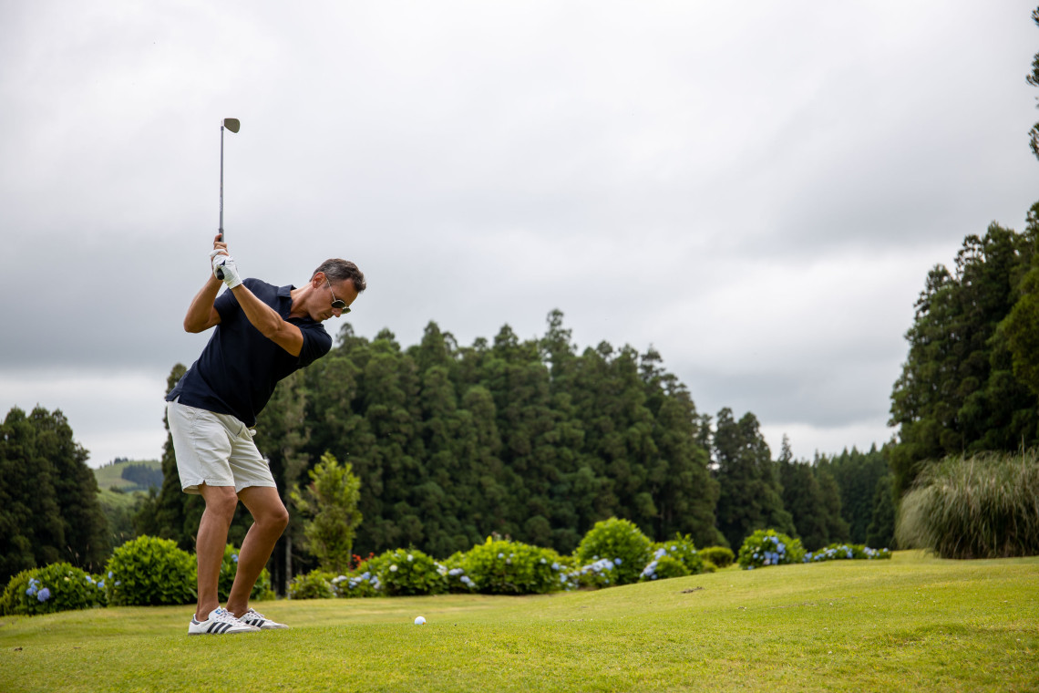 Golfer taking a swing on a green fairway in S&atilde;o Miguel Island, surrounded by hydrangeas, dense forest and the lush volcanic landscape of the Azores.