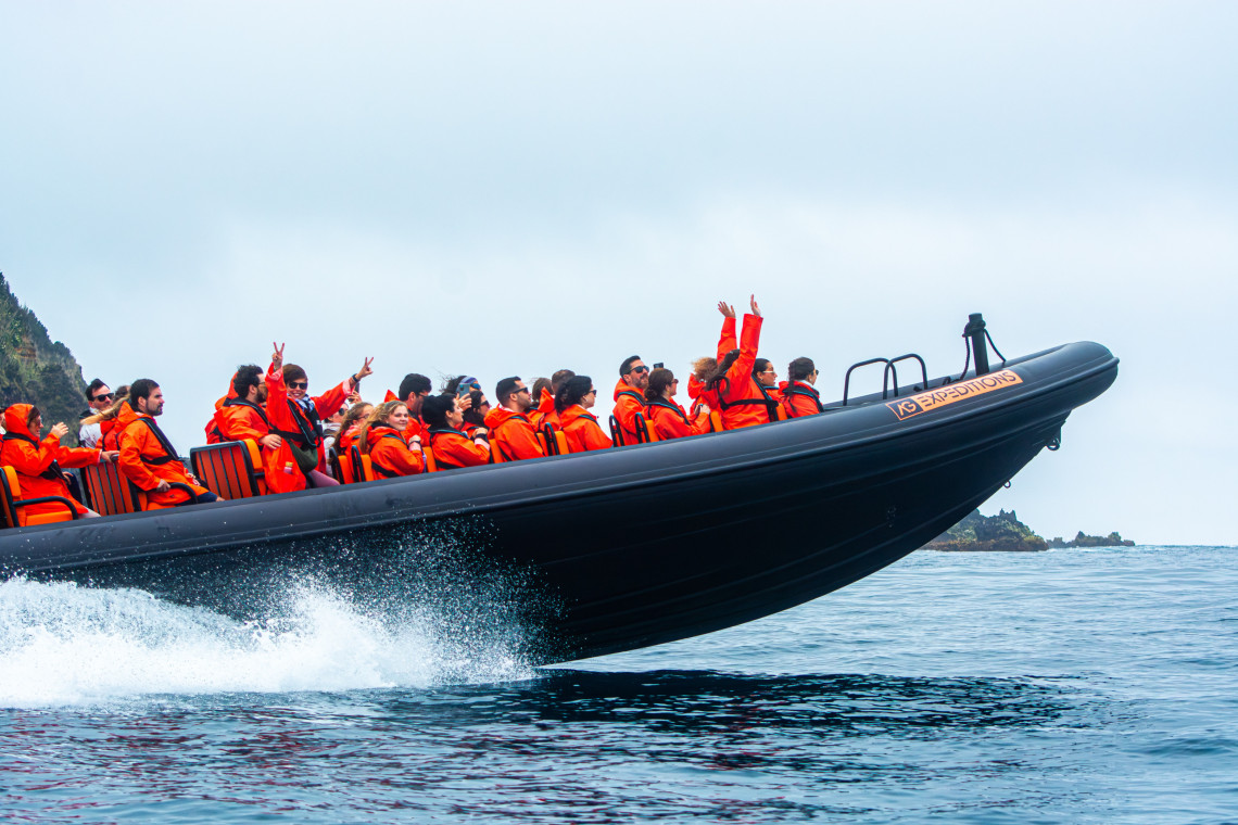 Grupo de personas en una lancha r&aacute;pida durante un tour en barco por la costa de S&atilde;o Miguel, Azores, con chalecos salvavidas naranjas y el oc&eacute;ano Atl&aacute;ntico de fondo