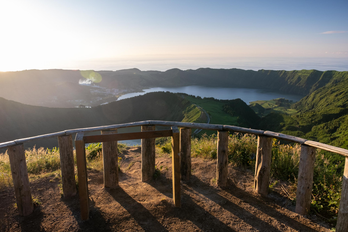 Sunset view from Miradouro da Boca do Inferno over the Sete Cidades caldera, with volcanic lakes, green ridges and the Atlantic Ocean visible beyond.