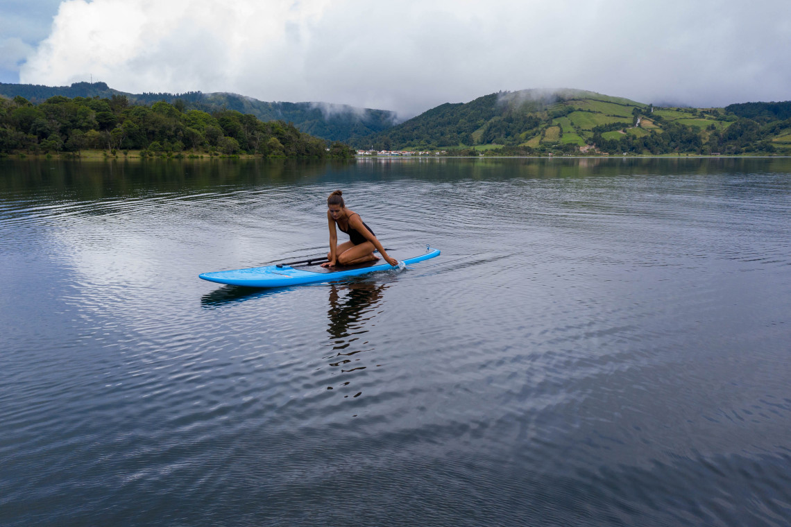 Visitor paddleboarding across the calm waters of Lagoa das Sete Cidades, surrounded by green hills and the forested walls of the volcanic caldera.