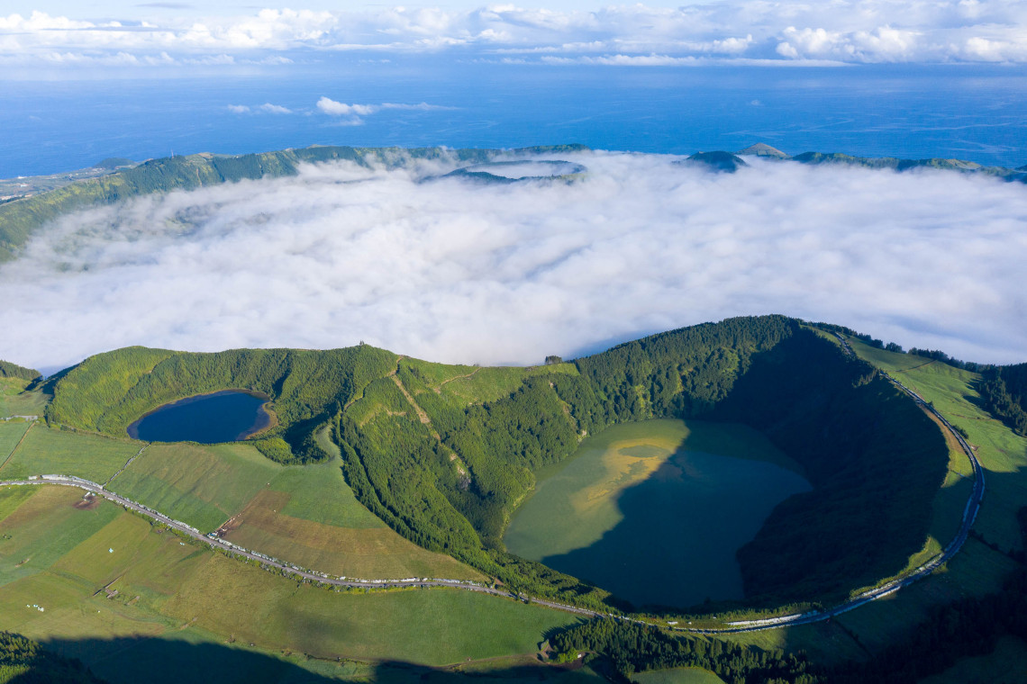 Aerial view of volcanic lagoons in the Serra Devassa area of S&atilde;o Miguel Island, surrounded by green crater rims, pastureland and low clouds.