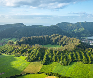 Aerial view of the green volcanic landscape around Sete Cidades on São Miguel Island, with cultivated fields, forested ridges and the caldera rising in the background.