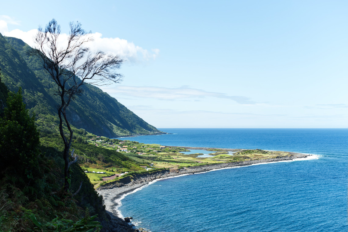 Elevated view of Faj&atilde; dos Cubres on S&atilde;o Jorge Island, showing its coastal lagoon, green fields and curved volcanic shoreline beside the Atlantic Ocean.