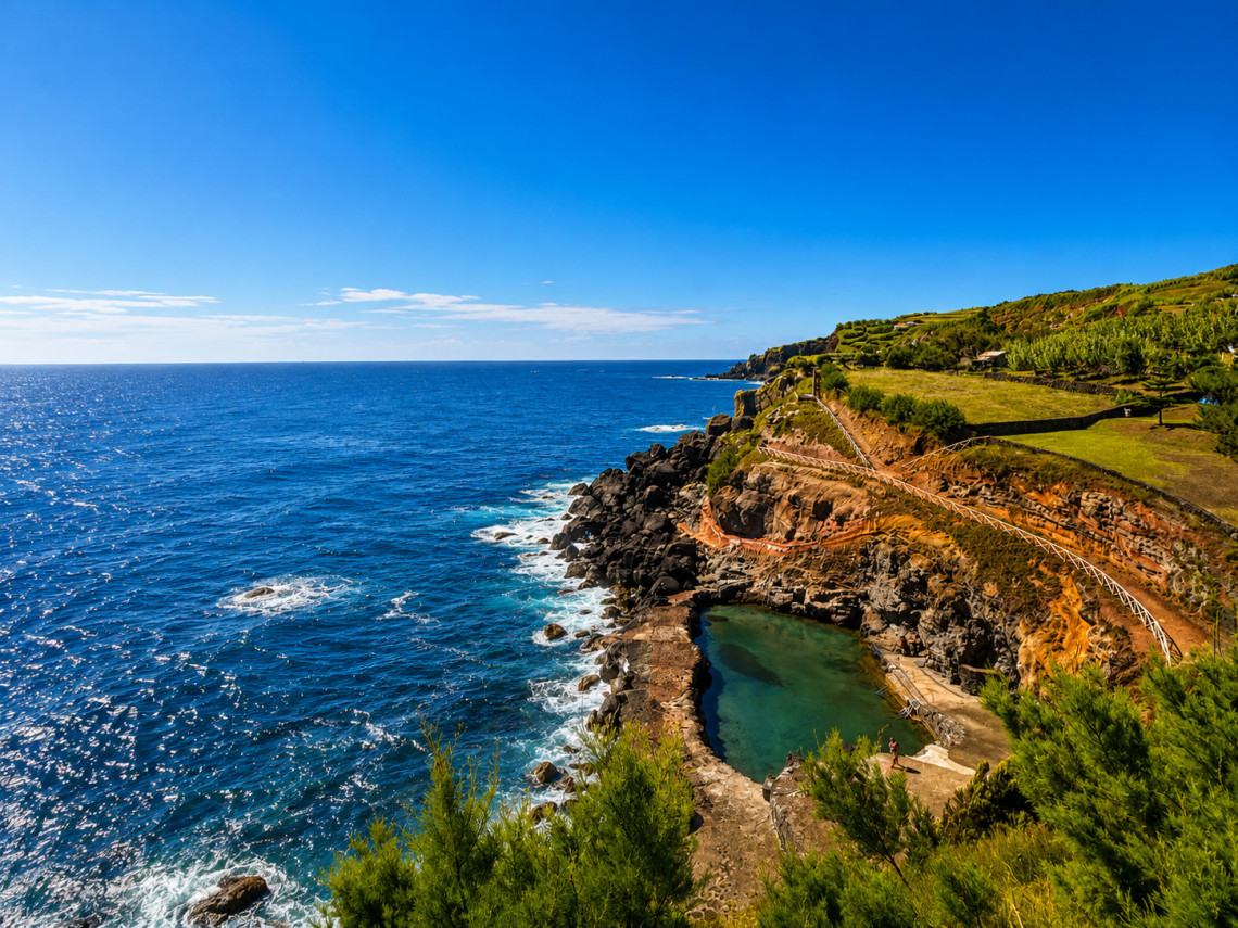 Natural swimming pool at Pontinha do Topo on S&atilde;o Jorge Island, set into reddish volcanic rock beside the Atlantic Ocean with a walking path descending toward the water.